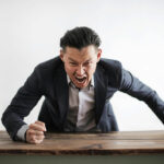 Angry man yelling and pounding his fist on a table.