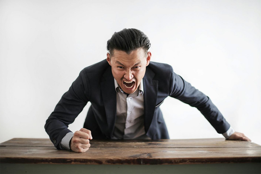 Angry man yelling and pounding his fist on a table.