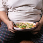 Close-up photo of an overweight man holding a bowl of food