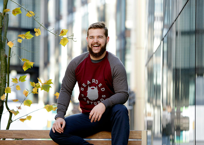 Man with a beard sitting on an urban park bench and laughing